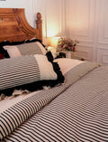 The Colette Cover Set by Uahan — black and ivory striped duvet cover with ruffled pillow covers, lamplit bedroom