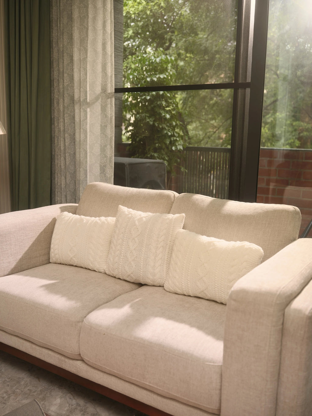 The Maman Cable-Knit Cushion Covers by Uahan — three ivory cable-knit cushions on a linen sofa by the window